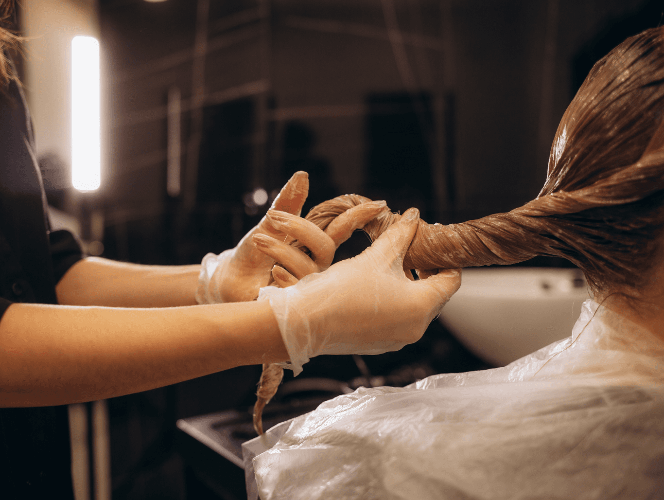A stylist wearing gloves carefully applying product to saturated hair during a colour correction process at The Dolls House salon in Eastbourne.