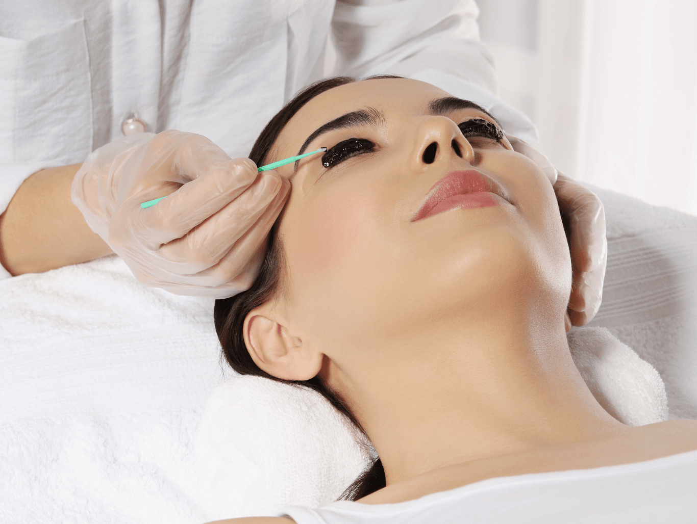 A beauty therapist applying dark tint to a client’s lashes during a professional eyelash tinting treatment at The Dolls House in Eastbourne.