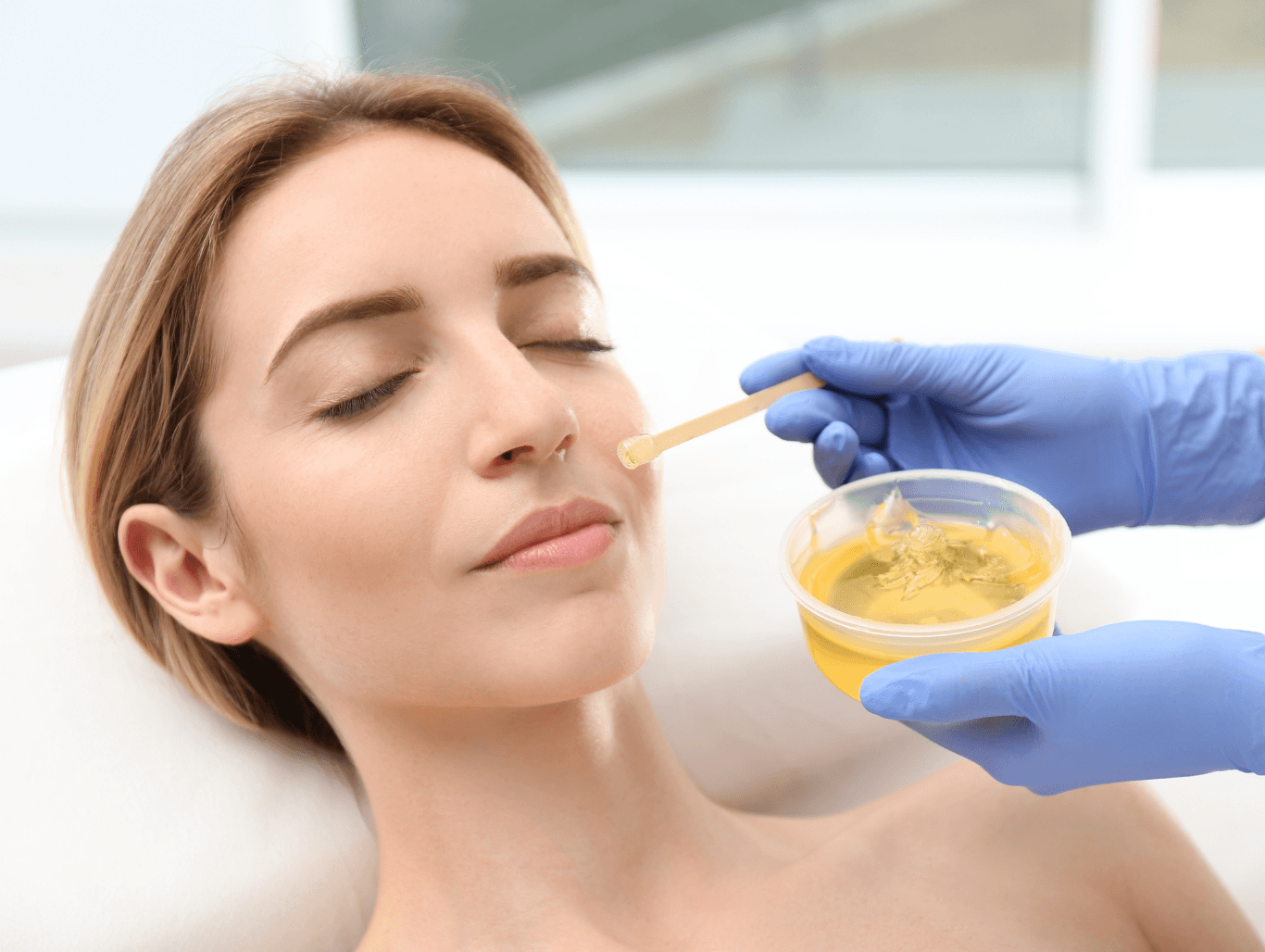 A beauty therapist applying warm wax to a client’s cheek during a full face waxing treatment at a professional salon in Eastbourne.