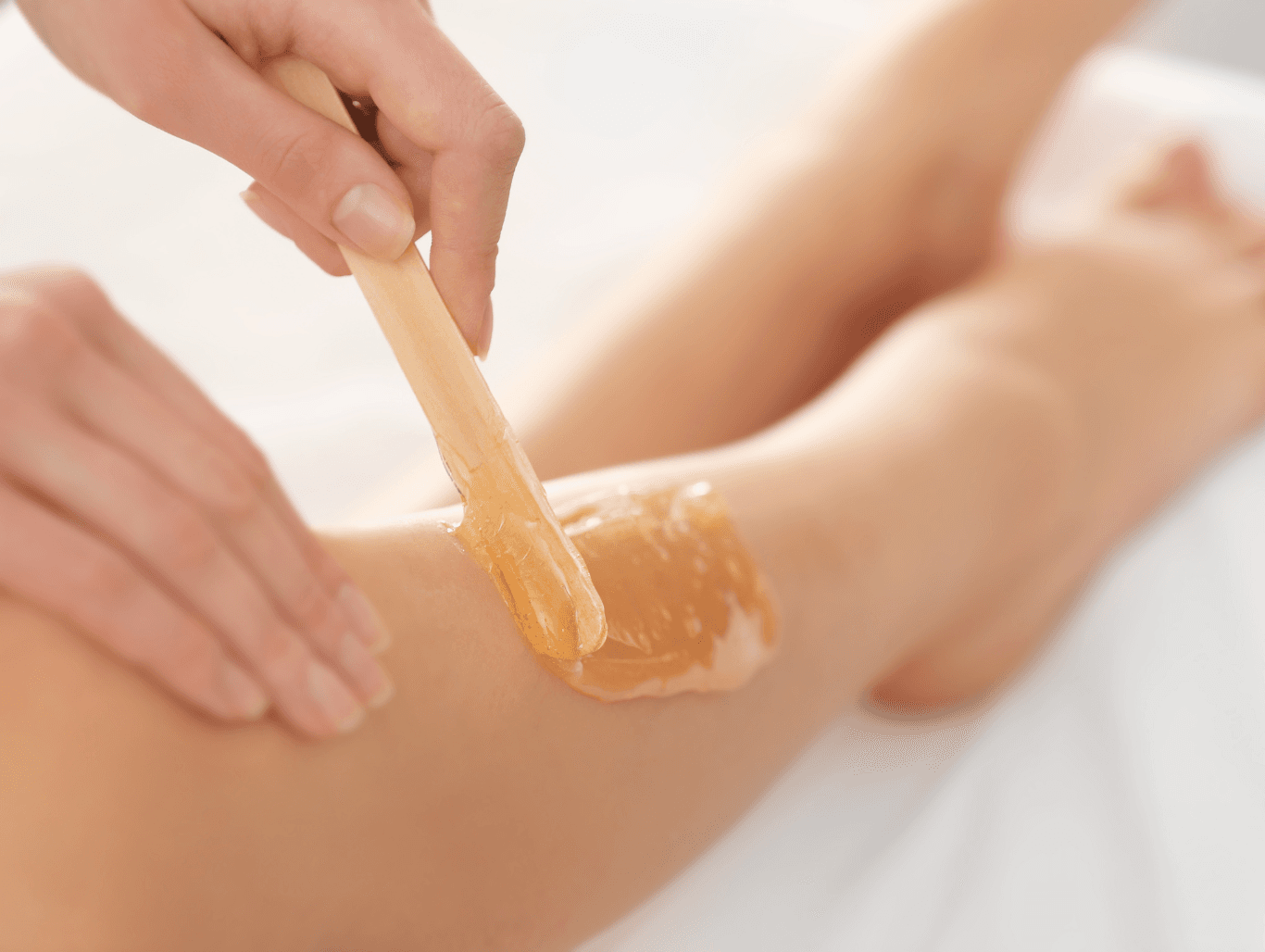 A beauty therapist applying warm wax to a client’s lower leg during a professional half leg waxing treatment at The Dolls House in Eastbourne.