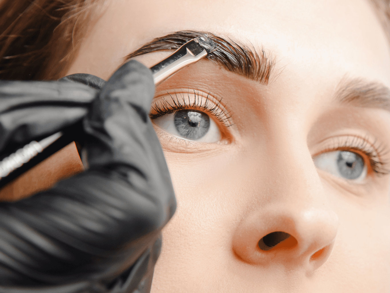 A close-up of a beauty therapist applying rich henna tint to a client’s eyebrows for fuller, defined results at a salon in Eastbourne.