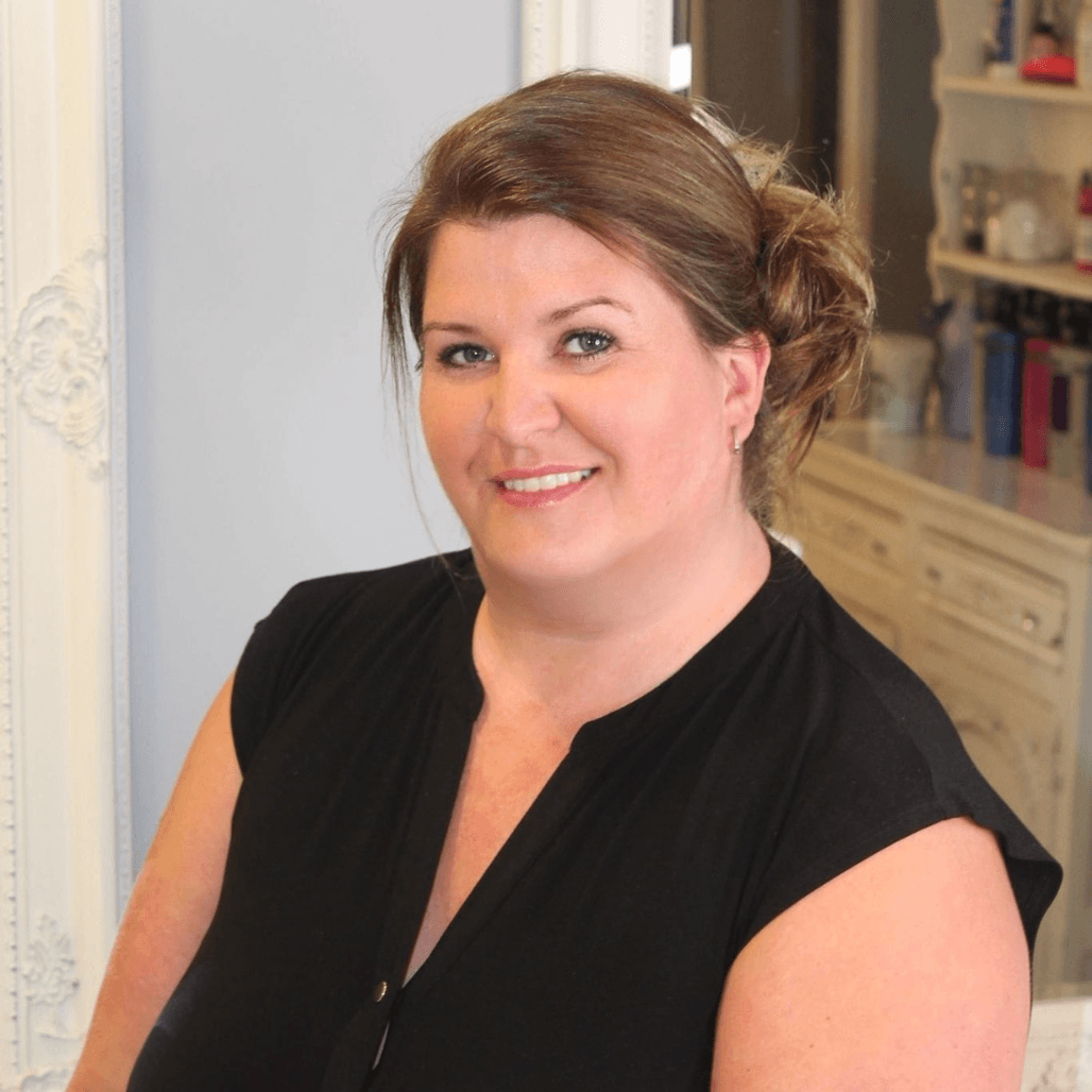 Lisa, an experienced hair stylist at The Dolls House in Eastbourne, smiling warmly inside the salon with classic décor in the background.