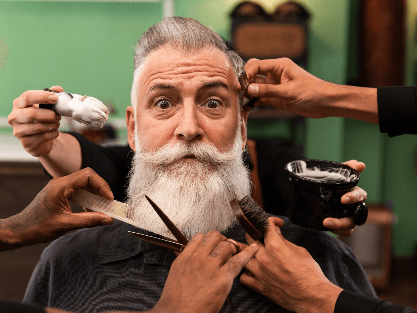 A cheerful senior gentleman with a white beard in a barbershop setting, receiving lighthearted, multi-handed grooming, capturing the fun and care of a men’s haircut for senior citizens at The Dolls House in Eastbourne.