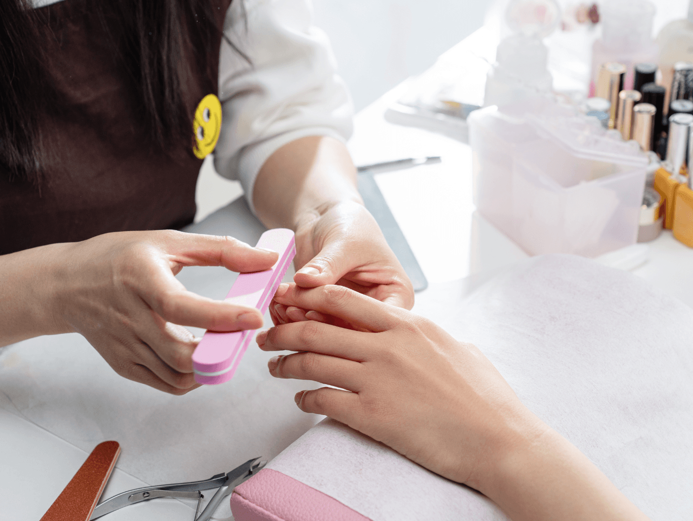 A young client receiving a gentle mini manicure, with a nail technician shaping the nails using a pink file in a calm, welcoming salon environment.