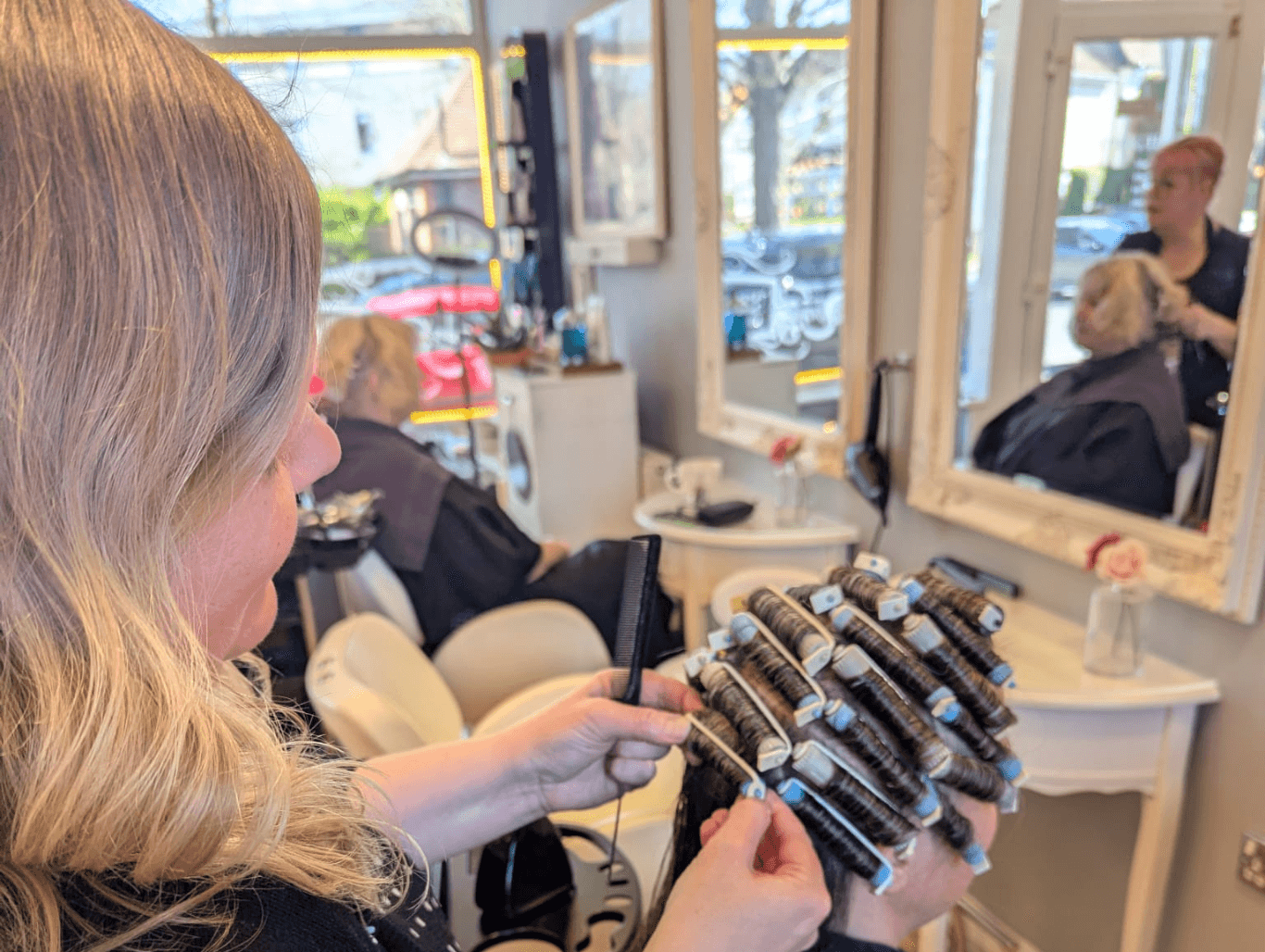A stylist at The Dolls House in Eastbourne carefully applying perm rods to a client’s short hair during a perming service.
