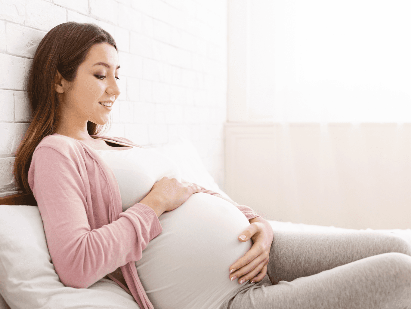 Pregnant woman relaxing on a bed, representing clients who benefit from pregnancy massage treatments.